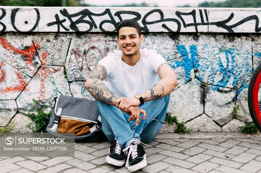 Smiling young man sitting at graffiti wall