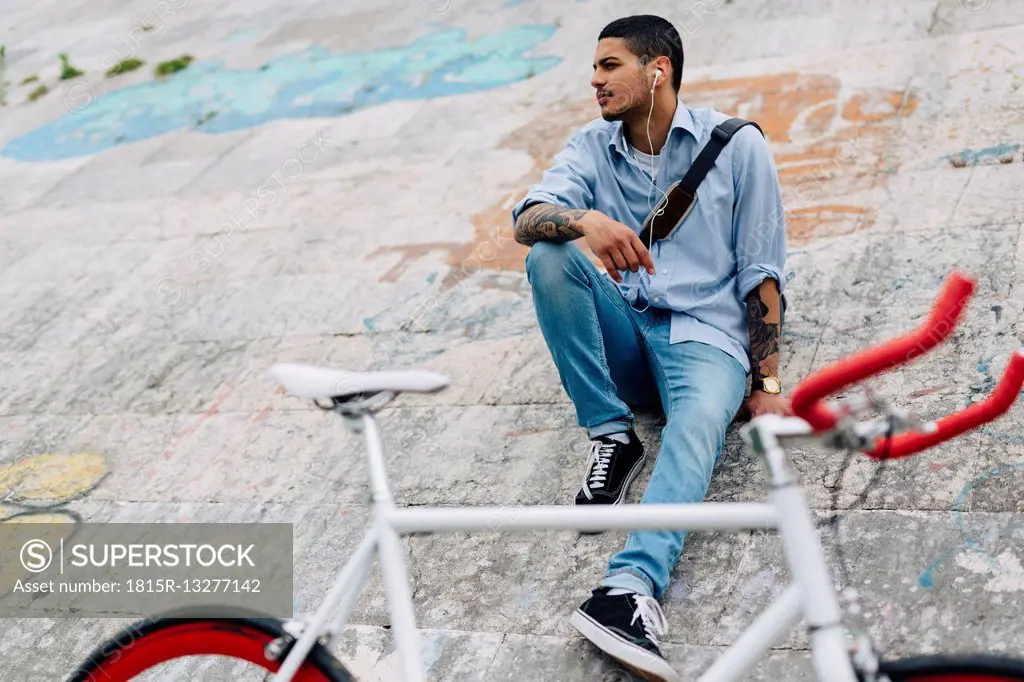 Young man with a bicycle sitting on a wall