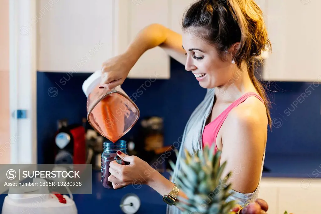 Smiling young woman in kitchen pouring smoothie into mug
