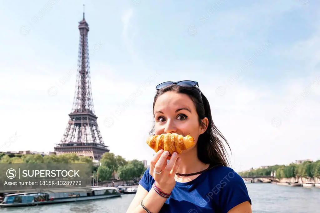 France, Paris, staring woman with croissant in front of Seine river and Eiffel Tower