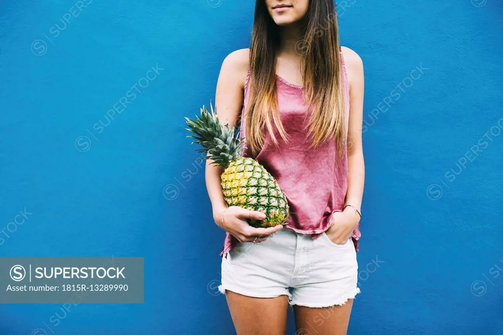 Young woman standing with pineapple at blue wall