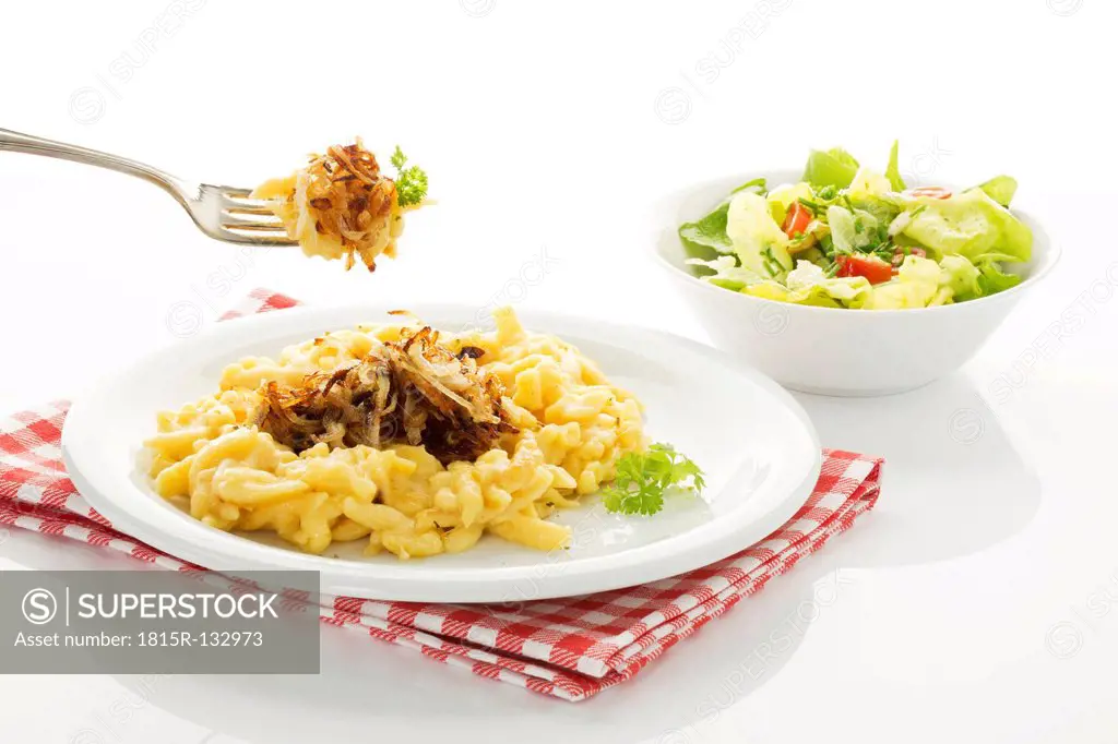 Plate of spaetzle with cheese and roasted onions besides salad bowl, close up