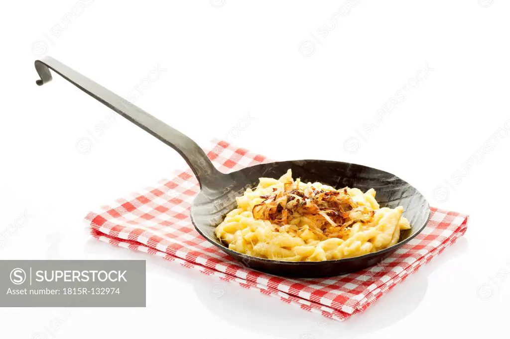Spaetzle with cheese and roasted onions in frying pan, close up