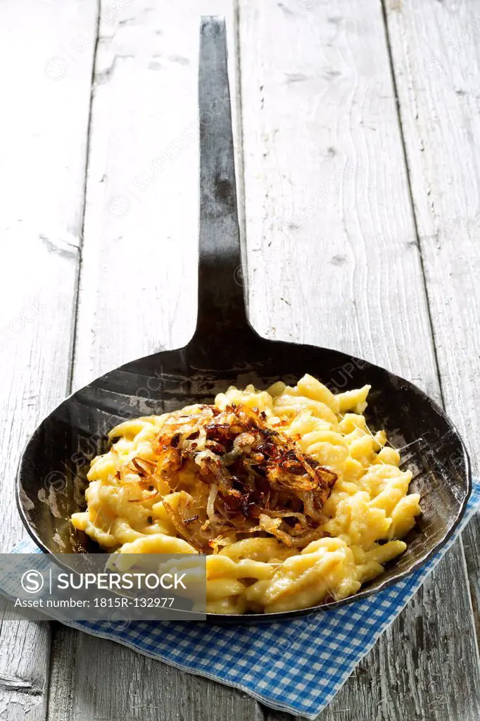 Spaetzle with cheese and roasted onions in frying pan on table, close up