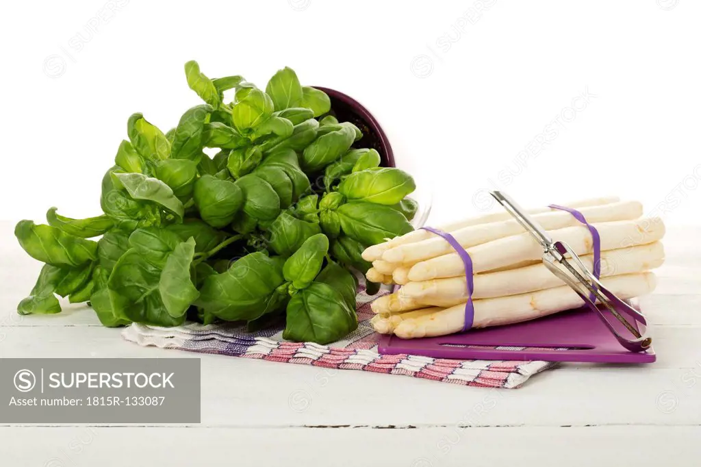 Bundle of white asparagus on chopping board besides basil plant