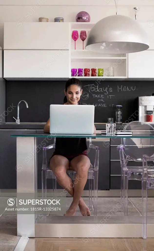 Young woman sitting at table in the kitchen working with laptop