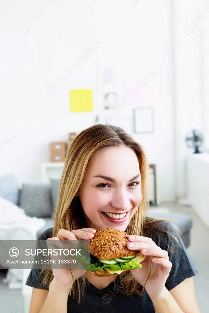 Germany, Bavaria, Munich, Portrait of young woman holding sandwich, smiling