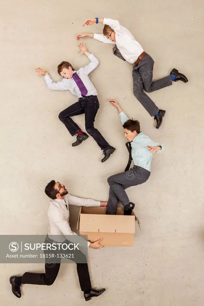 Businessman holding cardboard box while boys flying out