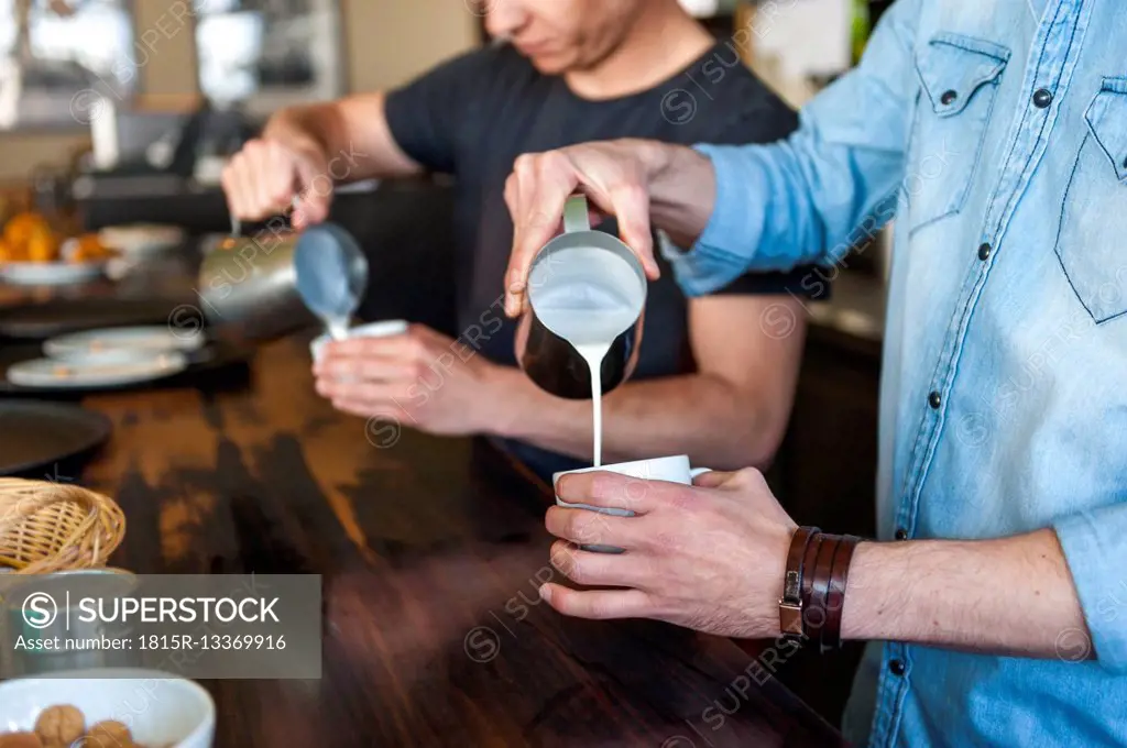 Two men preparing coffee with milk in a cafe