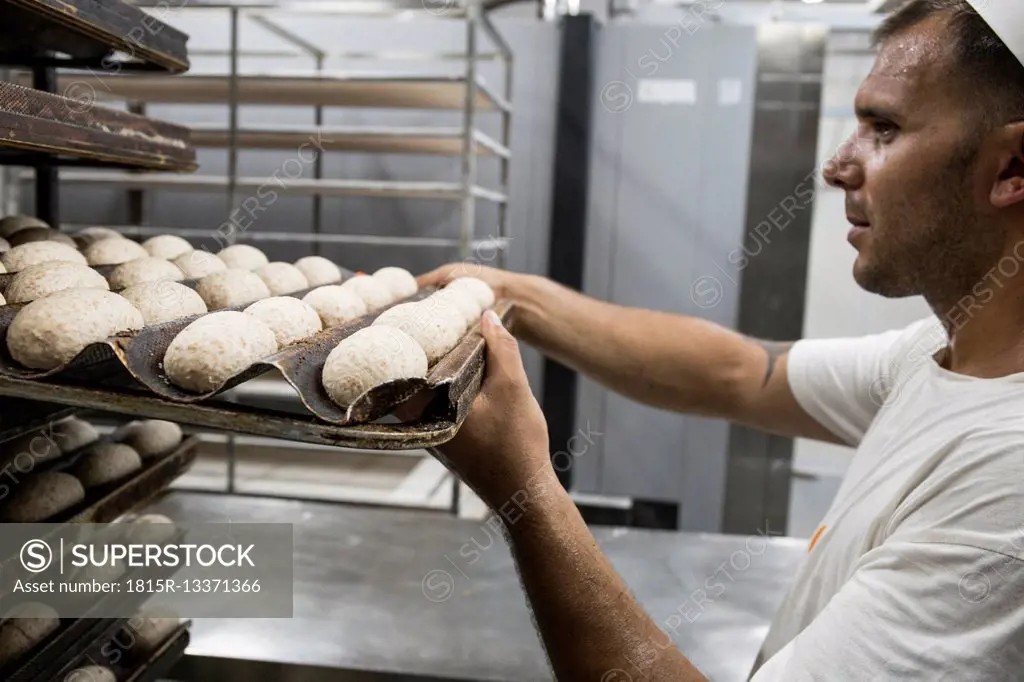 Baker placing a tray of bread dough in a bakery