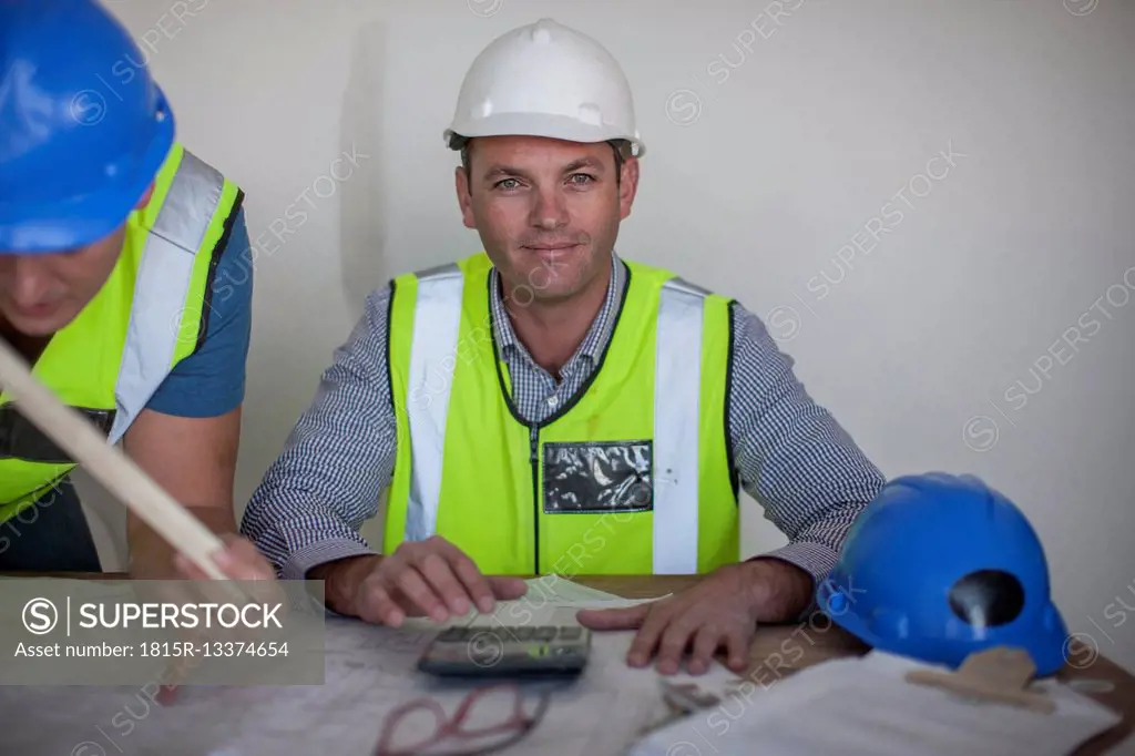 Confident architect with construction plan and calculator