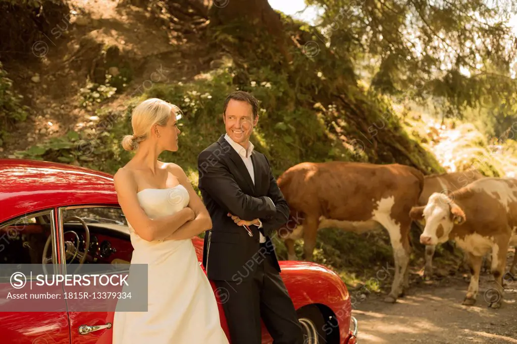 Bridal couple with vintage car waiting on a dirt track