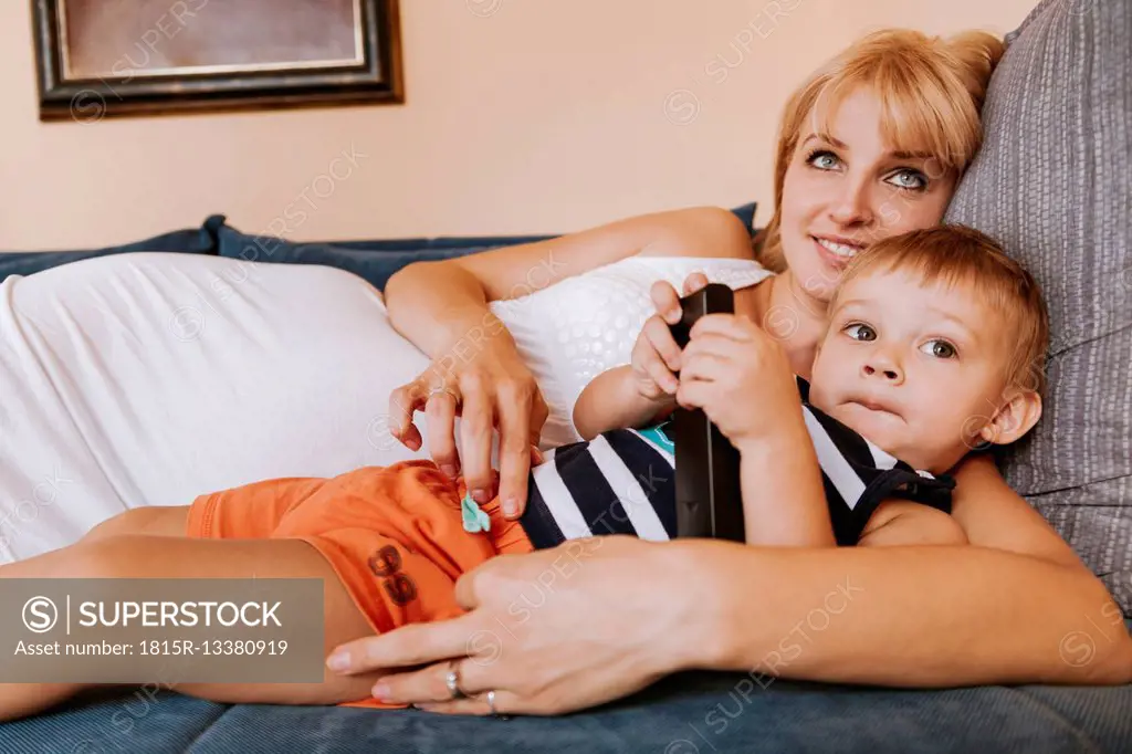 Pregnant mother and her little son lying on the couch watching TV