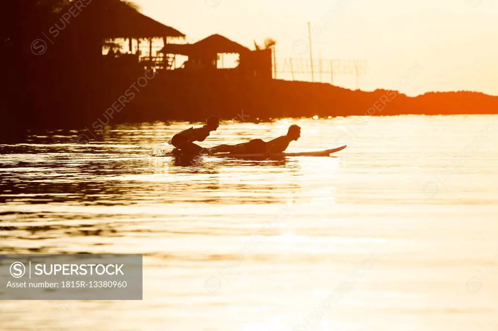 Thailand, couple doing yoga on paddleboard at sunset, cobra pose