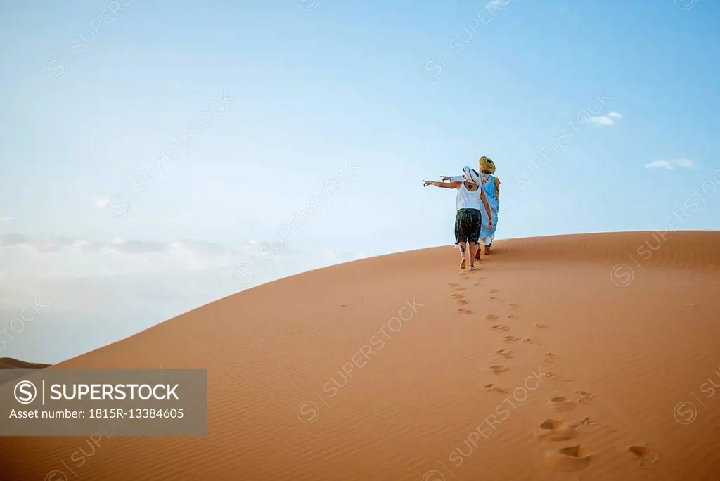 Berber man and woman tourist walking in the desert, pointing to the left