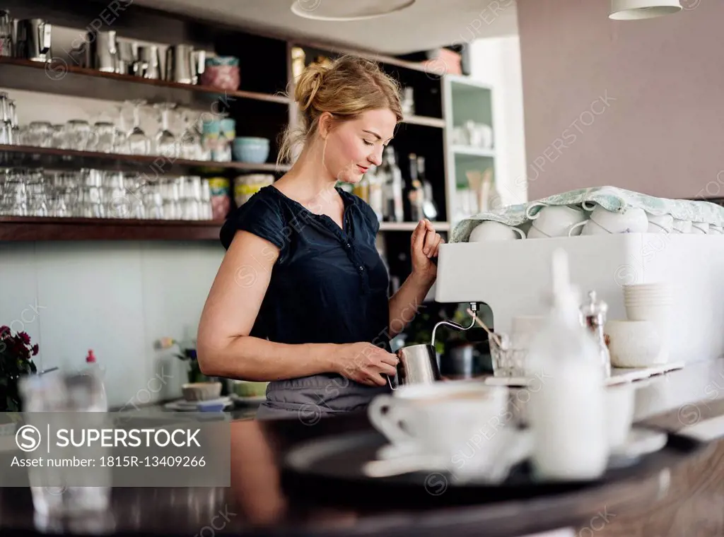 Woman in a cafe preparing milk froth for coffee