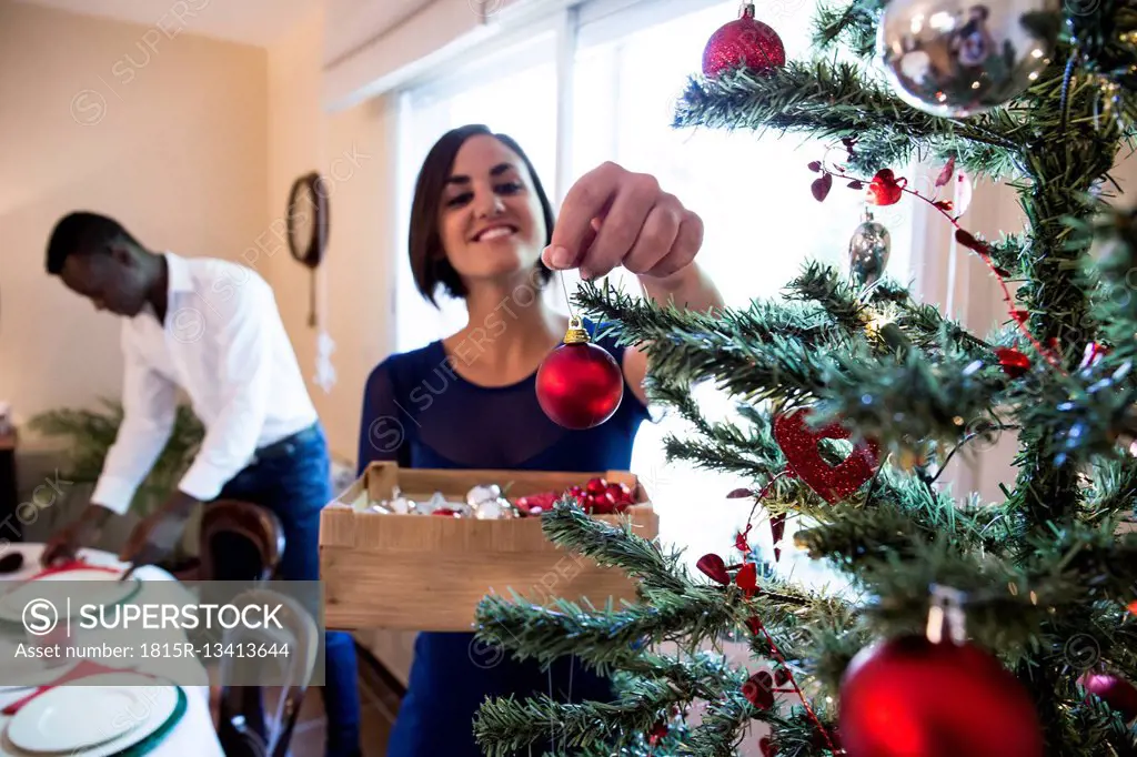 Woman decorating the Christmas tree with man in background