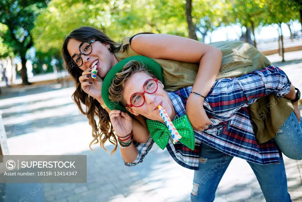 Young couple having fun with party blowers, joke glasses and caps