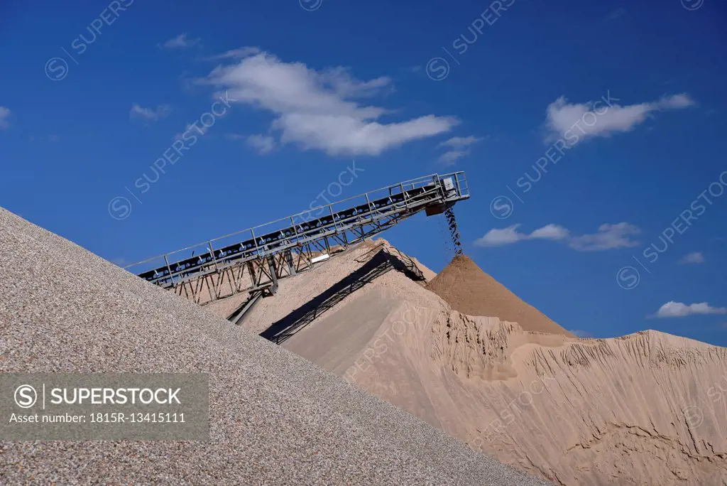 Conveyor belt pouring sand on heap in gravel pit