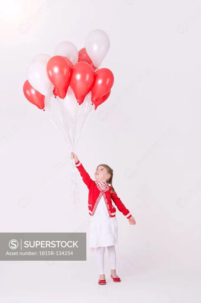 Girl holding bunch of balloons against pink background