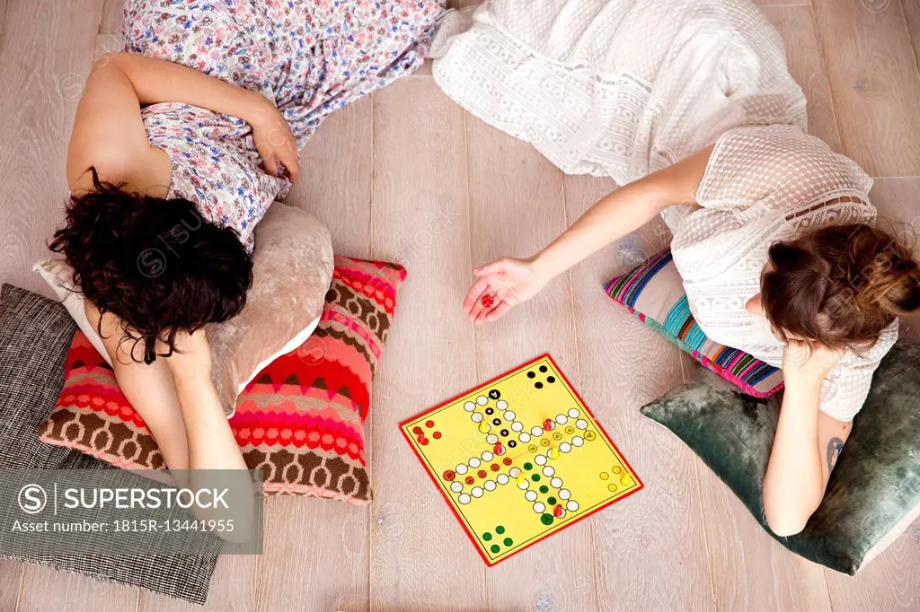 Top view of two best friends lying on the floor at home playing ludo