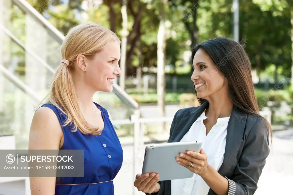 Two smiling women with digital tablet outdoors
