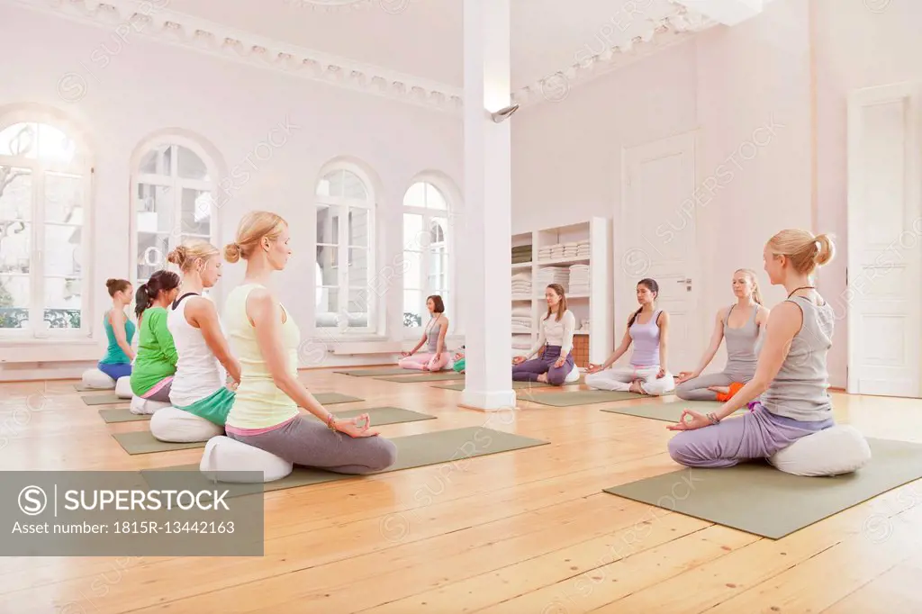 Group of women in yoga studio sitting in Lotus pose with instructor