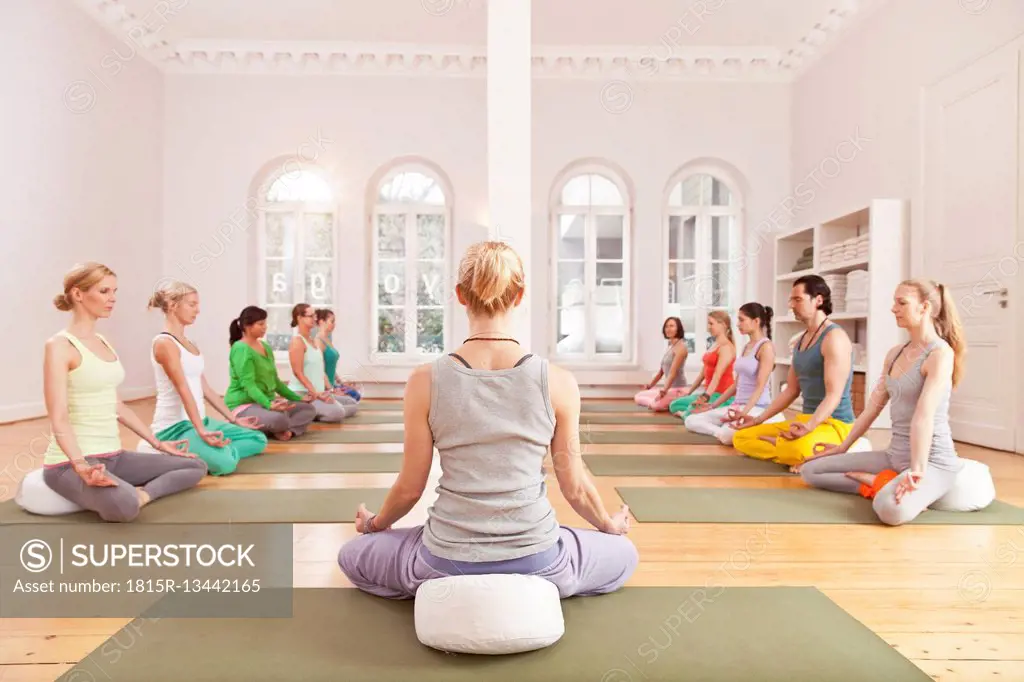 Group of people in yoga studio sitting in Lotus pose in front of instructor