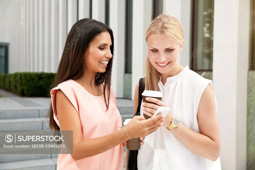 Two businesswomen with cell phone outside during a coffee break