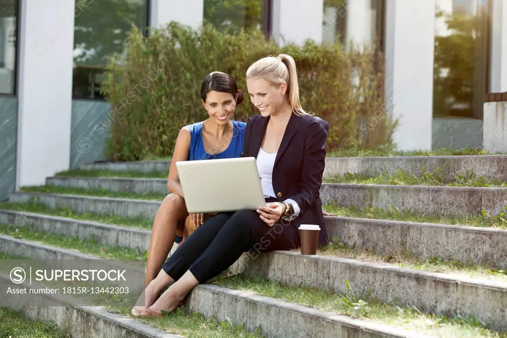 Two businesswomen sitting on stairs outside using a laptop
