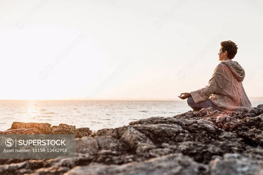 France, Crozon peninsula, woman meditating at beach at sunset