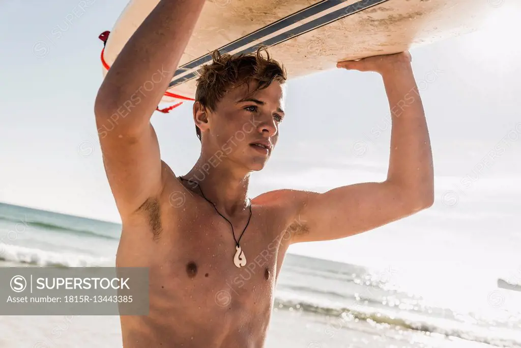 Teenage boy carrying surfboard at the sea