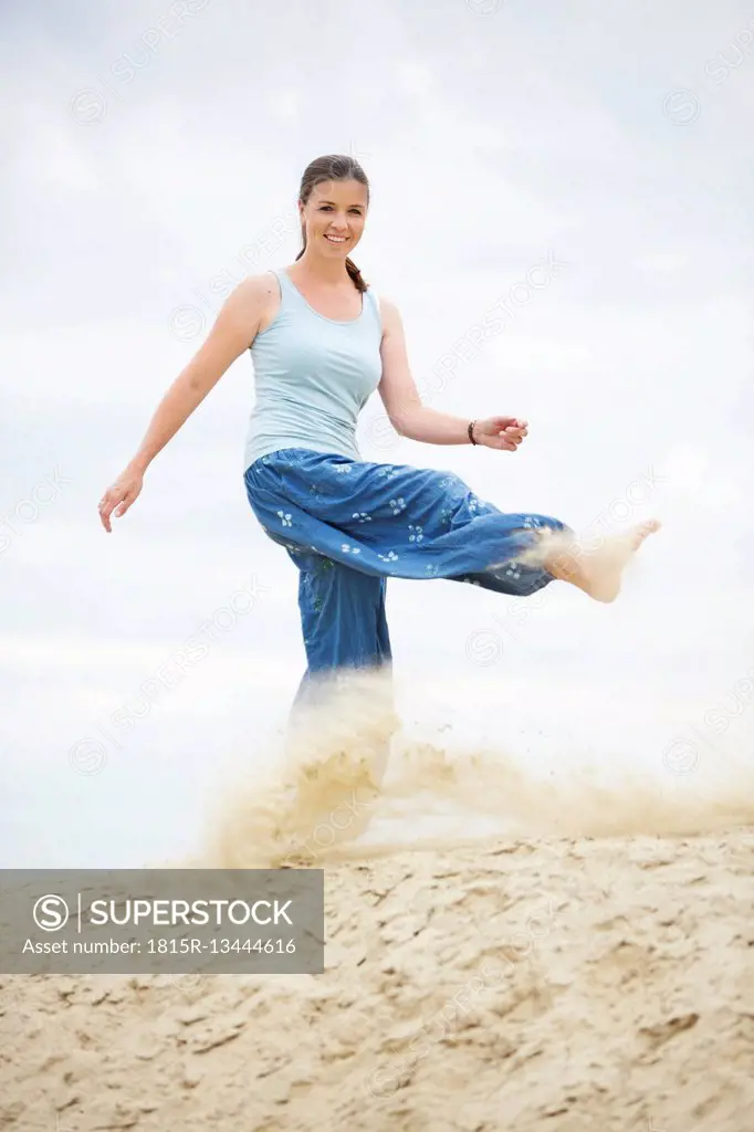Smiling young woman kicking sand
