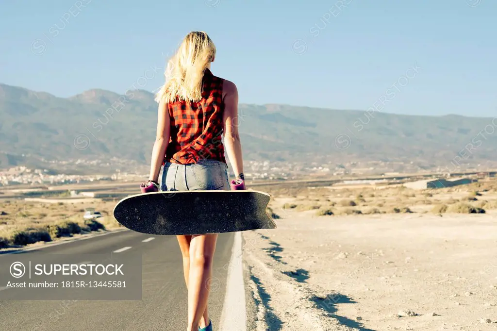Spain, Tenerife, blond young skater with skateboard walking on road