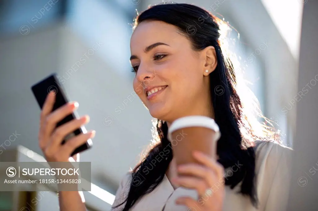 Smiling woman with takeaway coffee looking at cell phone