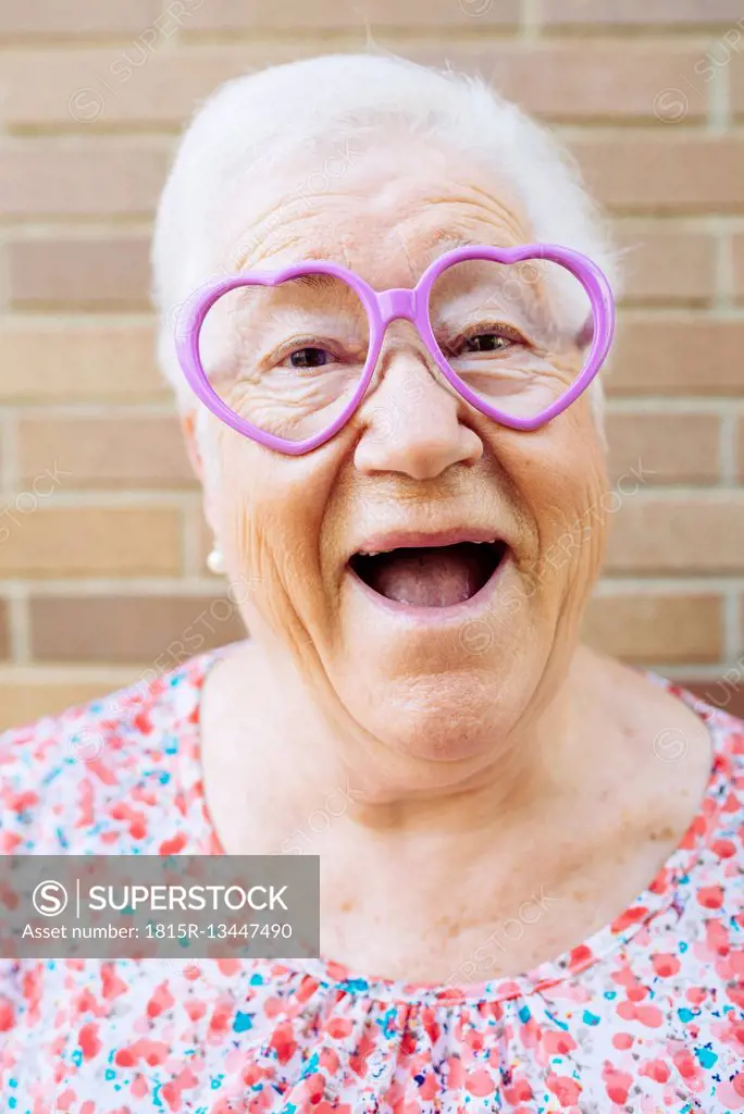 Portrait of happy senior woman wearing heart-shaped glasses pulling funny faces