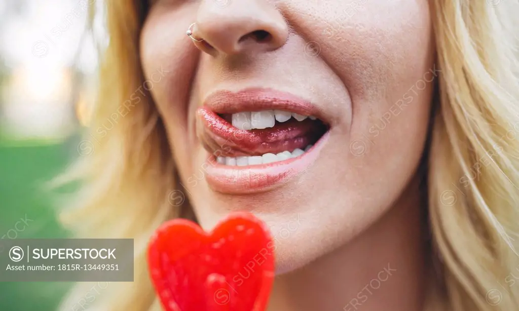 Close-up of young woman licking heart-shaped lollipop