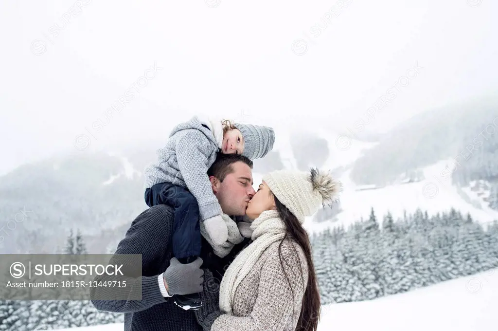 Couple with daughter kissing in winter landscape