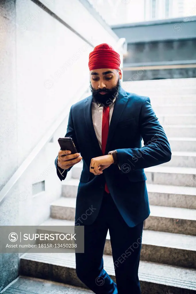 Indian businessman walking down stairs, looking at watch , holding smartphone