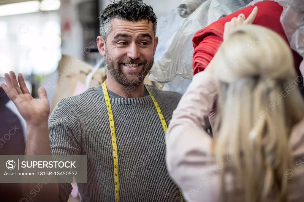 Smiling tailor looking at fashion designer in workshop