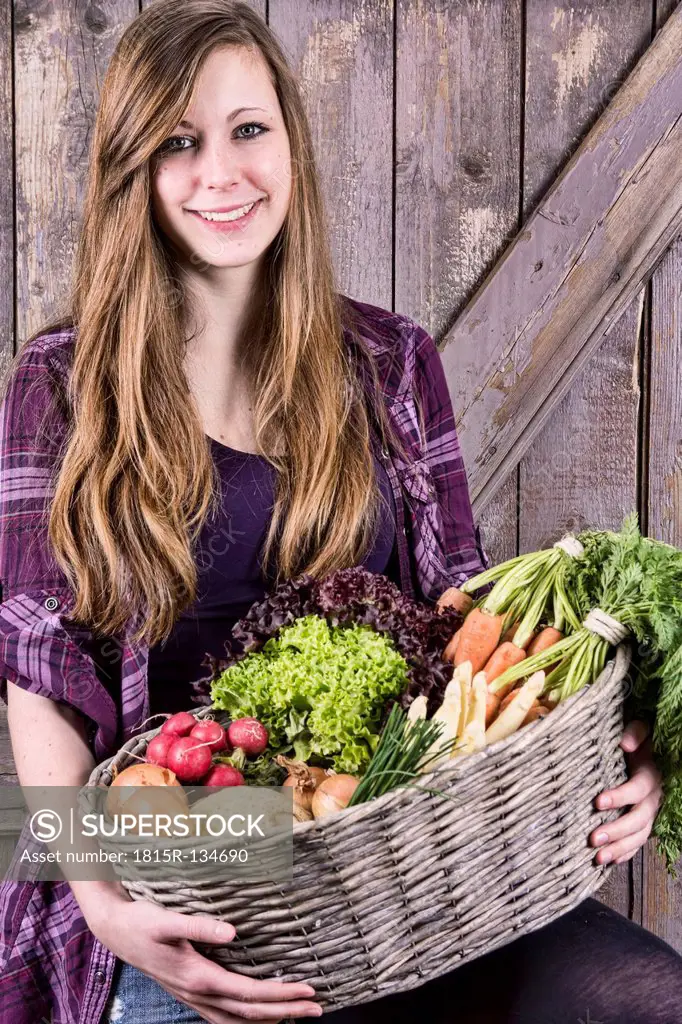 Germany, Portrait of teenage girl holding basket with organic vegetables, smiling