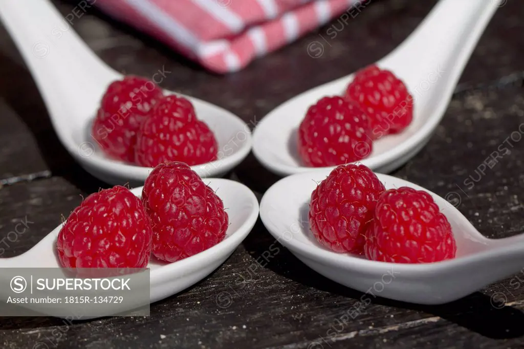 Fresh raspberries in white spoon on wooden surface
