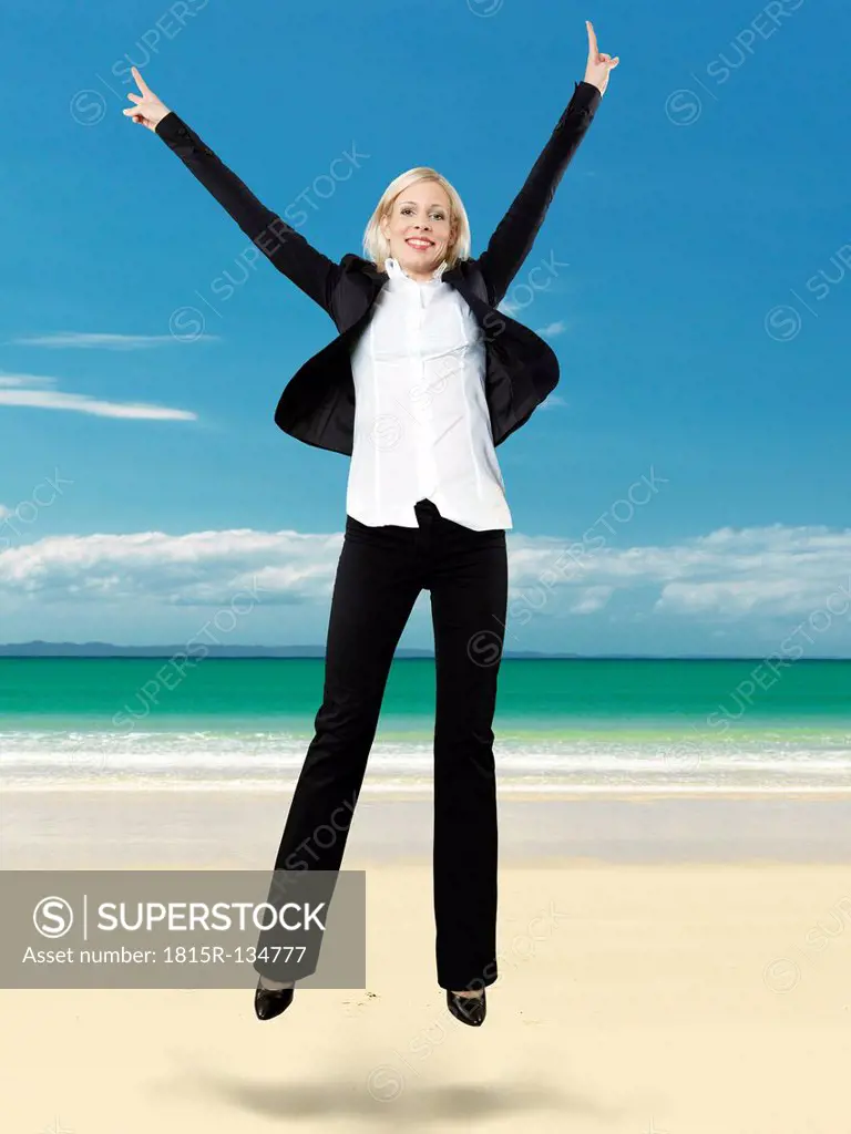 Portrait of businesswoman jumping on beach, smiling