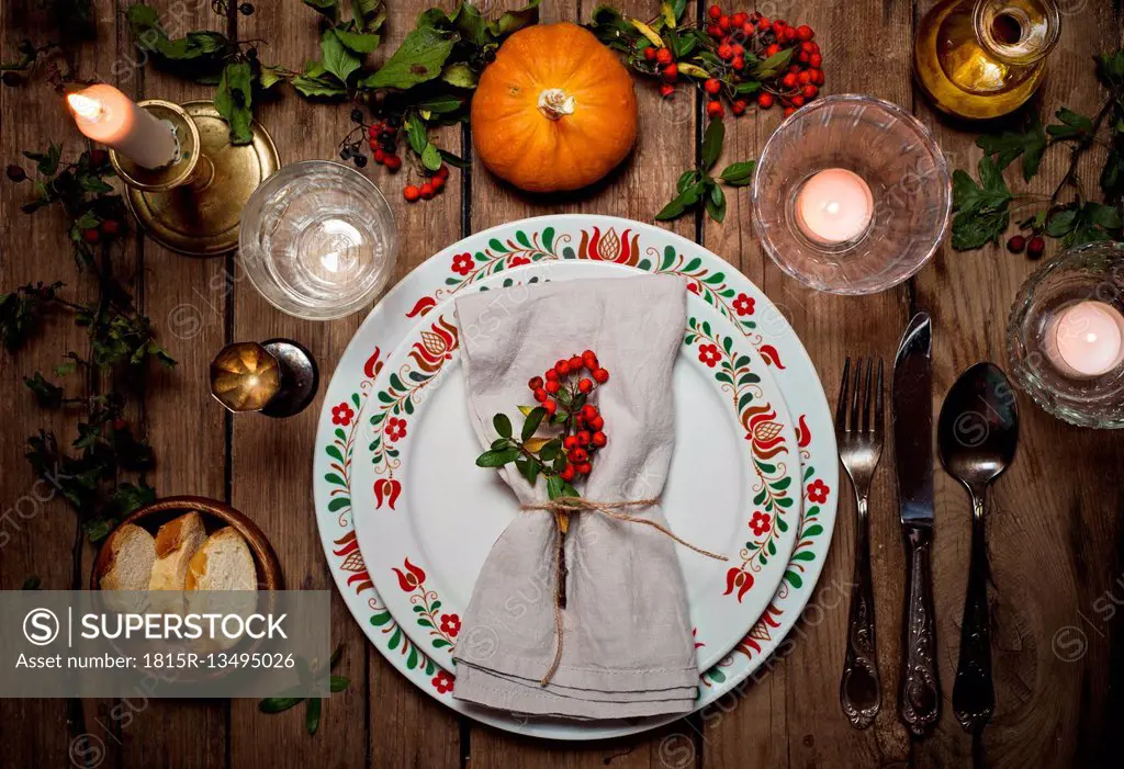 Autumnal laid table with pumpkin, holly and candle light