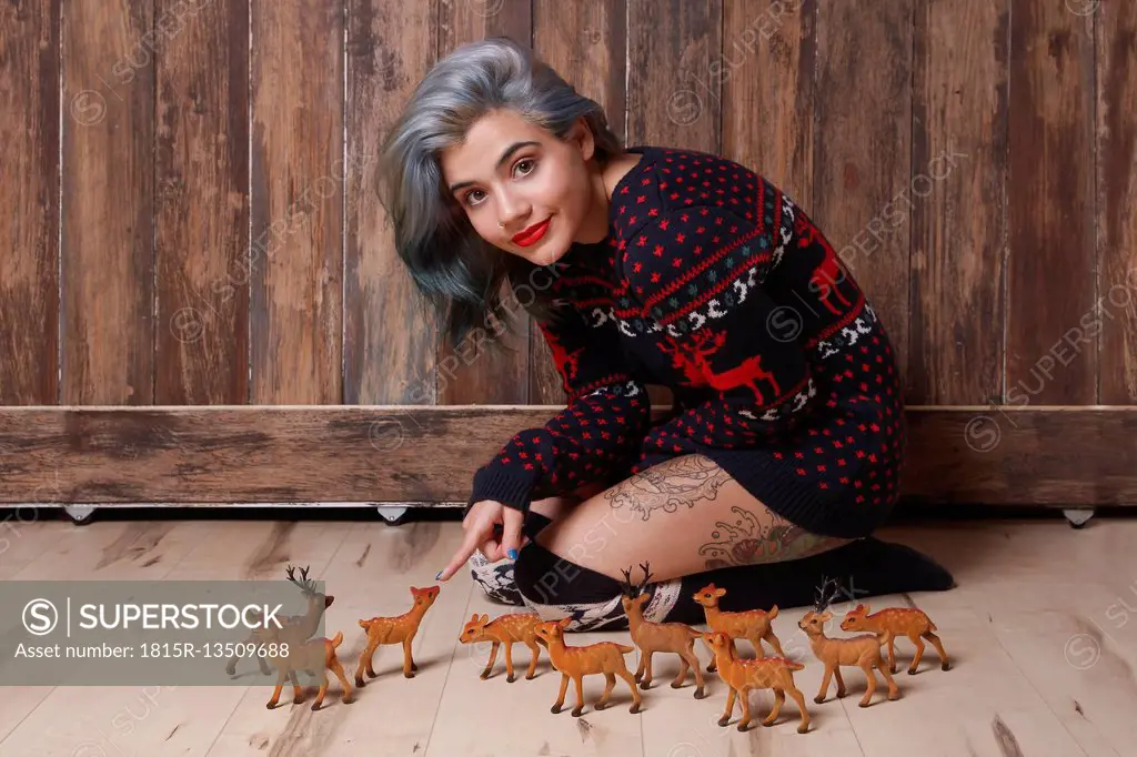 Portrait of smiling young woman wearing patterned knit pullover sitting on the floor with deer figurines