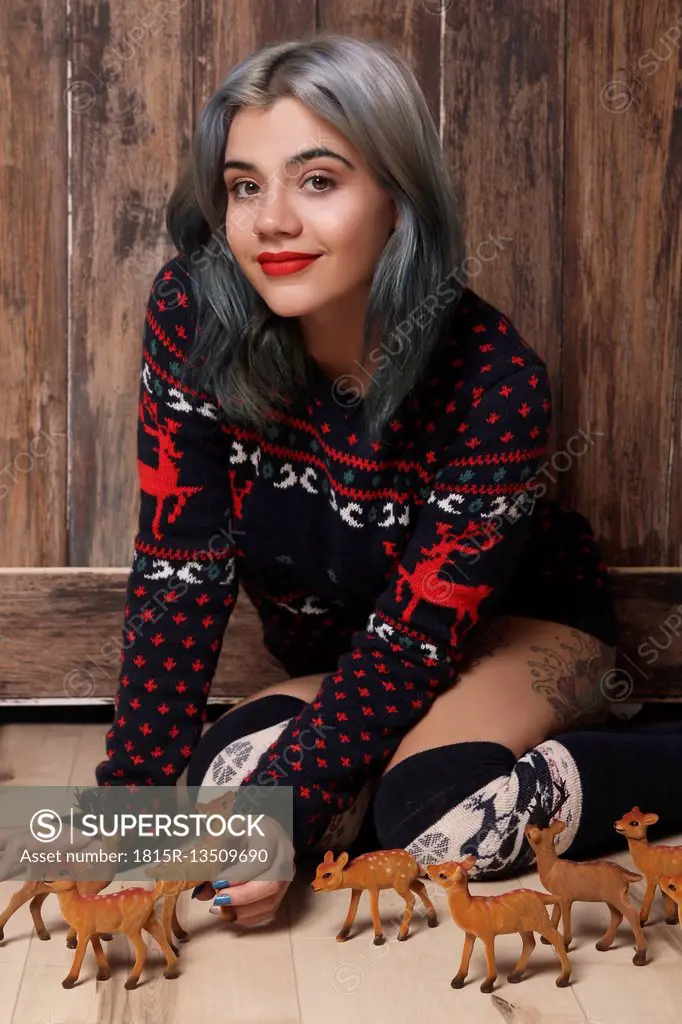 Portrait of smiling young woman wearing patterned knit pullover sitting on the floor with deer figurines