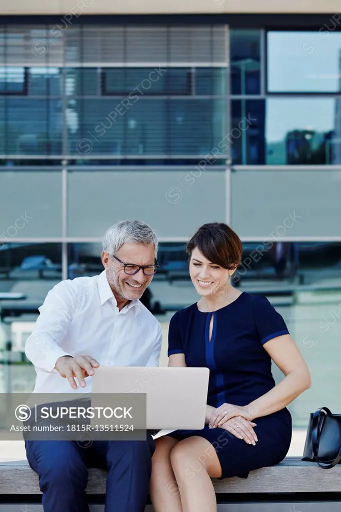 Businessman and businesswoman sitting on bench sharing laptop