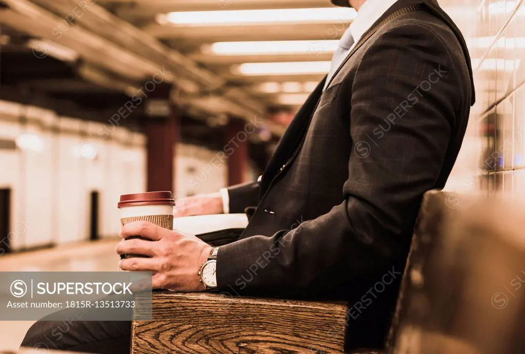 Young businessman waiting at metro station platform, holding disposable cup