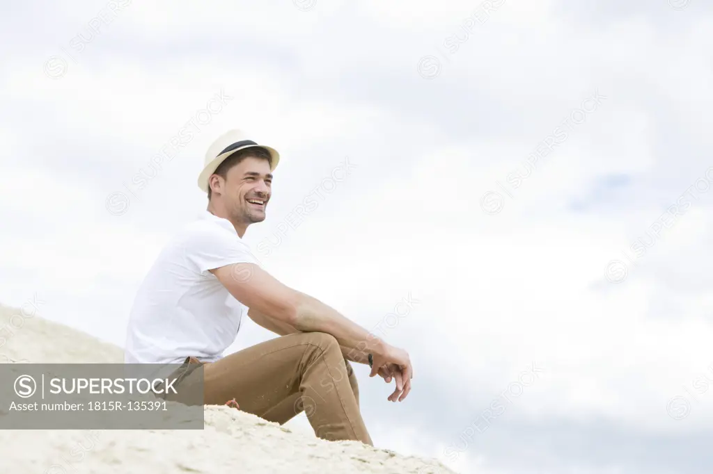 Germany, Bavaria, Young man sitting on sand, smiling