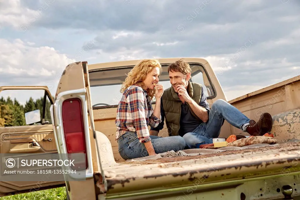 Couple sitting on pick up truck having a picnic